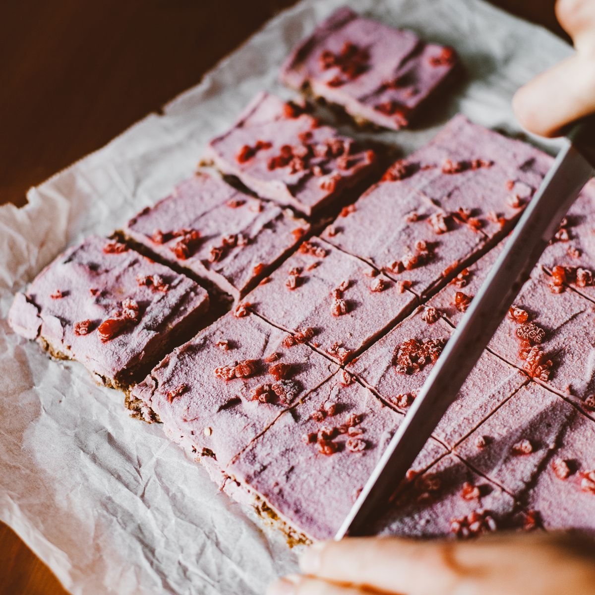 Gâteau rose découpé en parts carrées sur une feuille de papier cuisson
